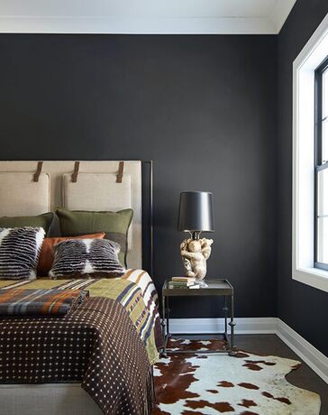 Black bedroom walls with a white and brown cow print rug underneath a tan bed with a printed comfort