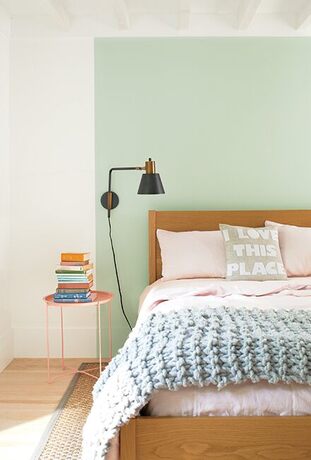 White bedroom with seafoam green color block behind wooden bed with light pink sheets and blanket.