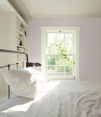 Large bedroom with light pink walls, white built in shelves, and a metal bedframe with white sheets.