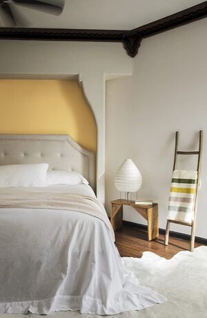 Off white walls with a yellow accent wall behind a tan bedframe with gray bedding. 
