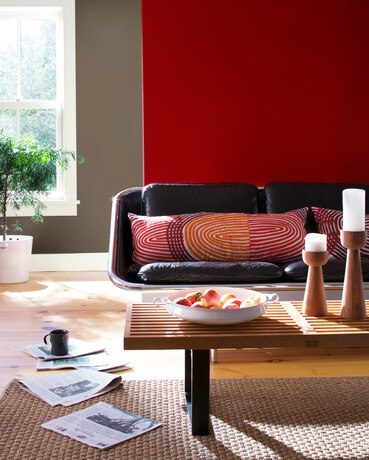 Casual living room with leather couch, wooden table, graphic prints, and bold red wall.