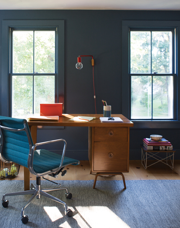 Mid-century modern office with blue walls, desk chair, rug, and wood desk.