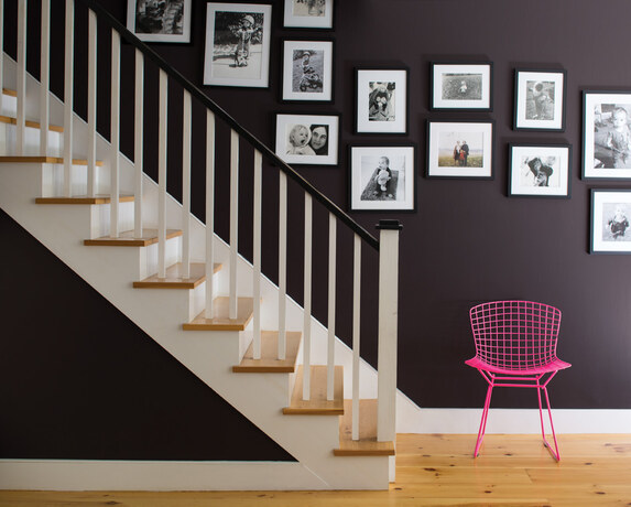 Staircase with black and white family photos, hot pink wire chair.