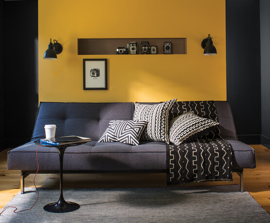 Gray couch, circular table, B&W patterned pillows against yellow accent wall.