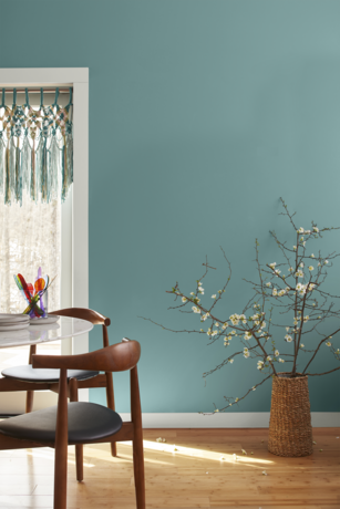 Teal-painted wall, macrame hanging, flowered branches, modern furniture, and hardwood floor.