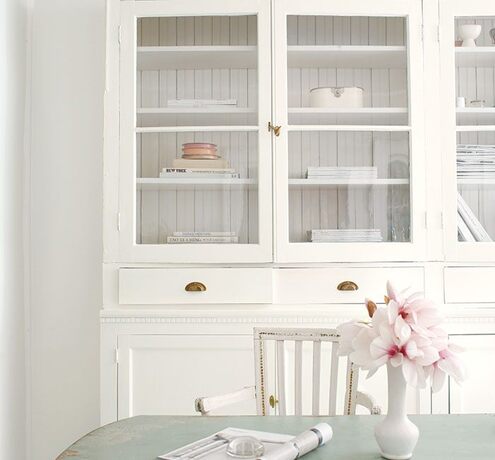 A shabby chic dining room with white walls, furniture, light-blue table, and gray floor.