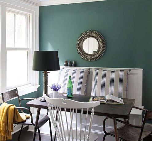 A cozy dining area with teal walls, white trim, banquette, mix of metal and white chairs