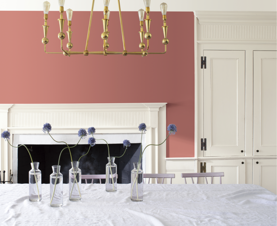 Light red-painted dining room with white cabinets, fireplace mantel, gold light, tablecloth