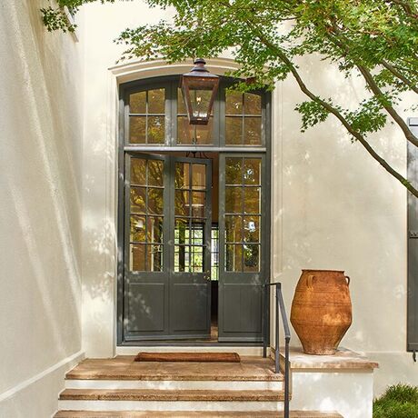An off-white painted stucco house with an elegant dark green front door with glass panes 