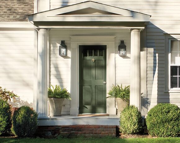 Una entrada cubierta y bonita de una casa pintada de blanco con una puerta delantera de color verde