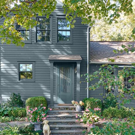 A nicely shaded, blue-gray painted house with blue doors and a picturesque front slate walkway 
