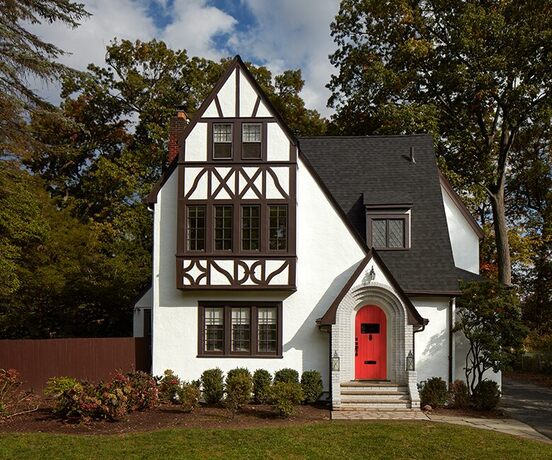 A charming tudor-style house with a red-painted front door, white exterior and dark brown trim
