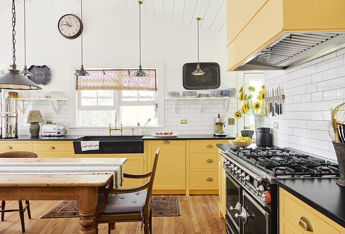 A bright, cheerful kitchen with white walls and yellow-painted cabinets, a wood table and wood floor