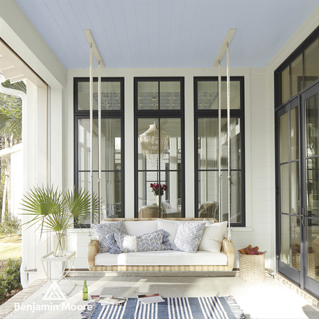 A white porch with window trim painted black, a white floor, blue and white area rug