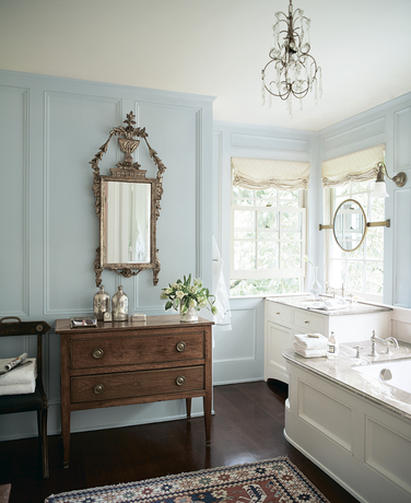 Un baño pintado de azul claro con espejo vintage y aparador.