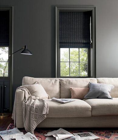 Sala de estar de color gris oscuro con molduras de ventana y un sofá color canela con almohadas.
