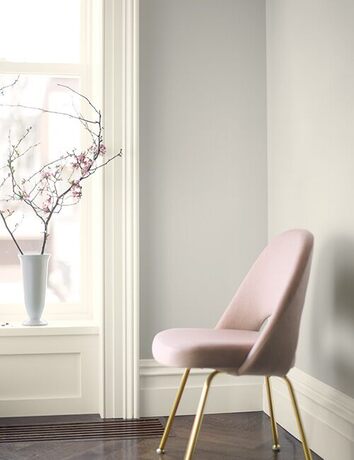 Una silla rosa contra paredes de color gris claro con adornos blanquecinos.