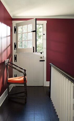 Puerta holandesa blanca, pasillo burdeos, silla naranja, piso madera oscura.