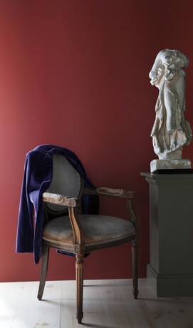 Una pared pintada de rojo intenso con una silla y una chaqueta morada junto a una columna gris.