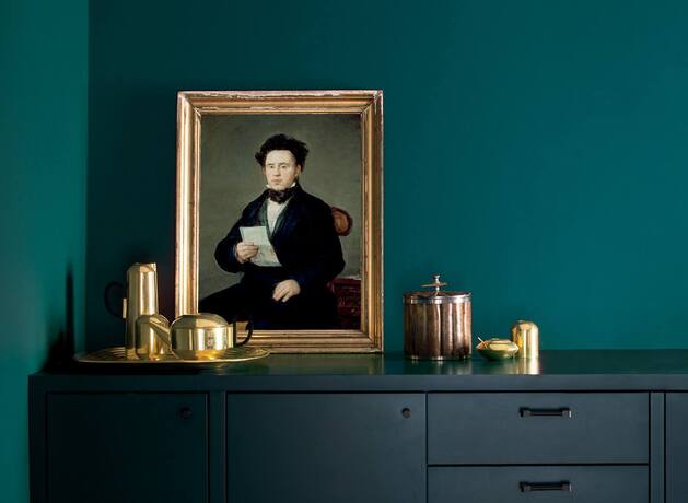 Una habitación pintada de verde intenso, con un retrato antiguo y un aparador pintado de azul marino