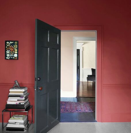 Una pared de color granada con una puerta abierta pintada de gris oscuro y una mesa con libros.