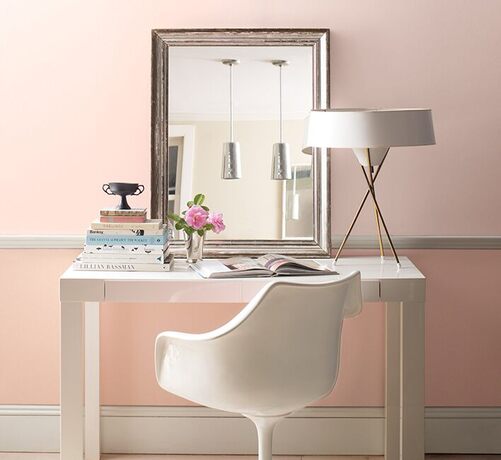 Two-toned pink-painted walls with a leaning mirror above a white desk and chair.