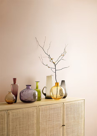 A credenza featuring a variety of colorful vases and branches in front of a pink-painted wall.