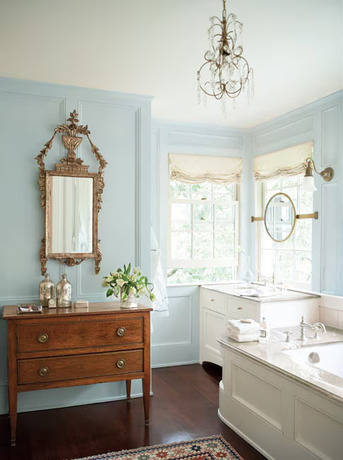 A classic bathroom with blue-painted walls, large white tub and matching sink, ornate mirror.