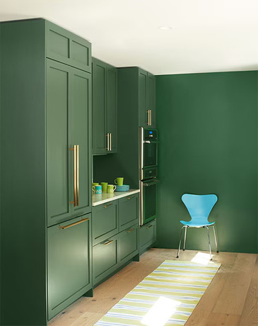 Green-painted kitchen with floor-to-ceiling cabinets, oven, and blue chair.