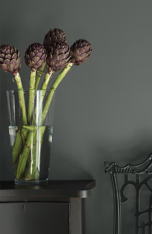 A black monochromatic scene with chair, simple table, and vase of green stems and aubergine flowers