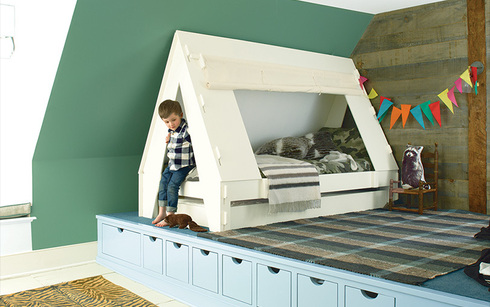 A green-painted angled wall frames a platform with a little boy and his tent bed.
