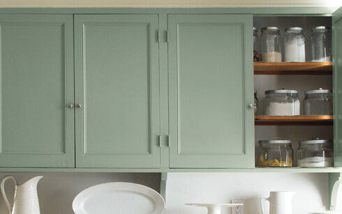 Light green cabinets add a soft glow as a backdrop to a dining table.