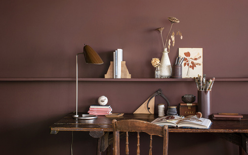 Una oficina con paredes pintadas de marrón, un estante largo de madera y un escritorio y una silla 