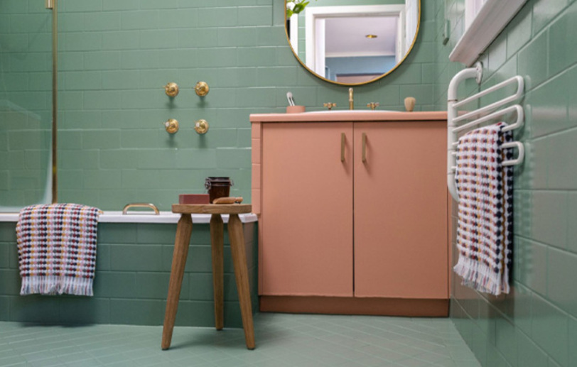 Los azulejos del baño están pintadas de color verde, hay una silla y un armario rosa.