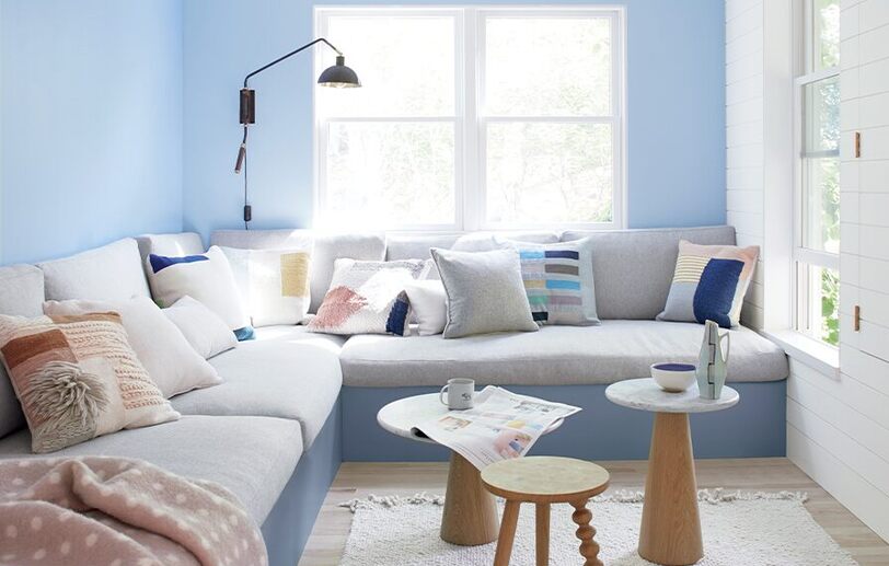 Sala de estar azul y blanca con seccional gris y 3 mesas auxiliares.