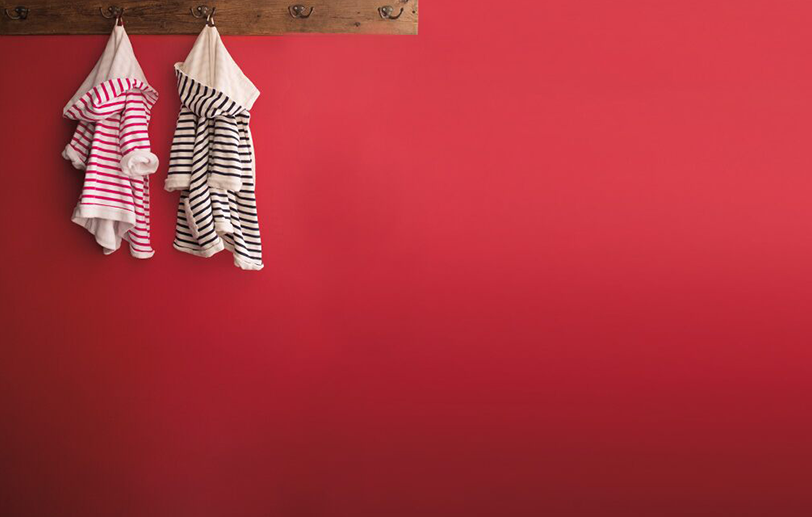 Red wall with a wooden plank coat rack, two striped children's robes, one in pink and one in black.