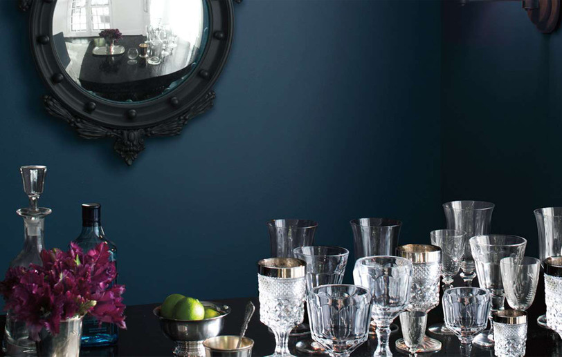 Una habitación pintada de azul oscuro con un espejo con marco negro y vasos de cristal 