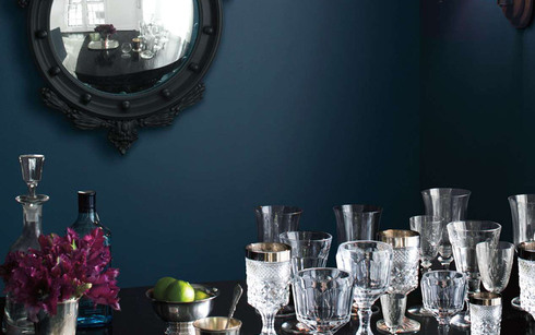Una habitación pintada de azul oscuro con un espejo con marco negro y vasos de cristal 