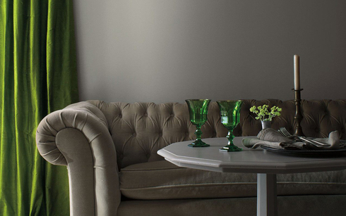 Una sala de estar con paredes pintadas de gris, un sofá gris y una mesa gris con detalles en verde.