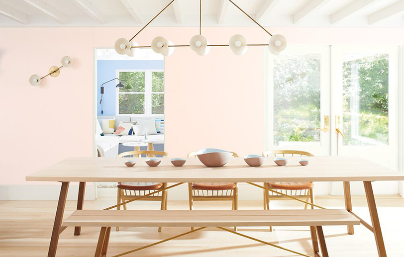 Paredes del comedor pintadas de rosa claro con una larga mesa de madera, sillas a juego y asientos d