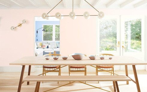 Paredes del comedor pintadas de rosa claro con una larga mesa de madera, sillas a juego y asientos d
