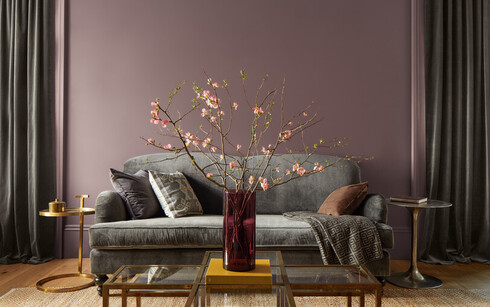 A purple living room has a gray couch, gold side tables, and a glass coffee table